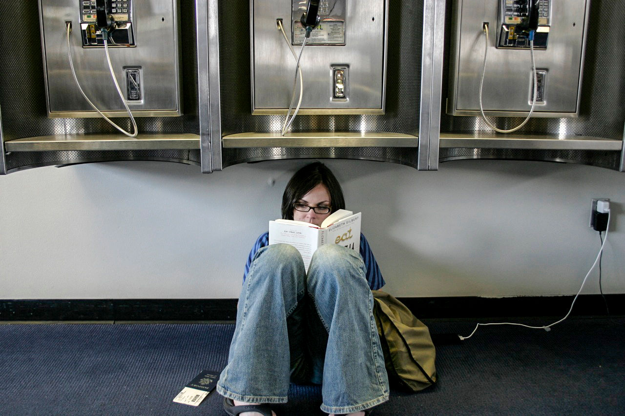 Woman charging her phone while sitting under payphones