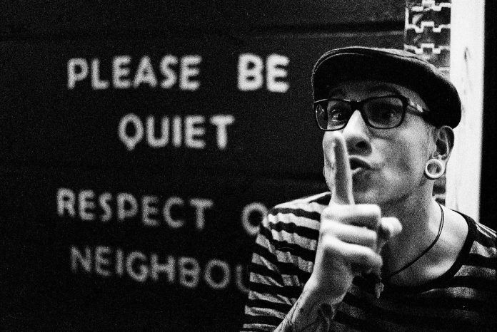 Please be quiet written on a wall with a male making a shh motion with hands