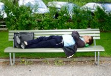 Man in a suit laying on a park bench asleep