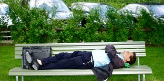 Man in a suit laying on a park bench asleep